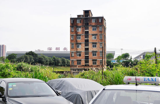 2016年6月13日，广东深圳，深圳龙华新区深圳北站附近，一栋墙体裸露红砖、显得破旧的七层小楼，孤零零地伫立在空地上，犹如一座孤岛，与远处的高楼形成巨大的反差。来源：光明网DIV